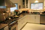 A contemporary pure white kitchen with stainless steal pulls and a black granite countertop.